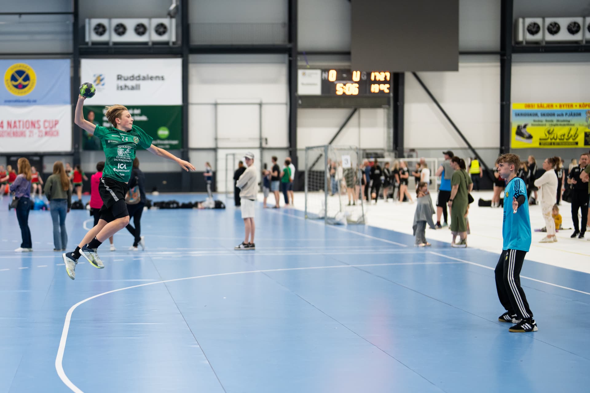 Ung handbollsspelare hoppar och skjuter under en cupmatch i en hall full av lag och publik